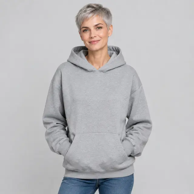 An adult woman with short silver hair wears a plain heather-gray hoodie in a studio.