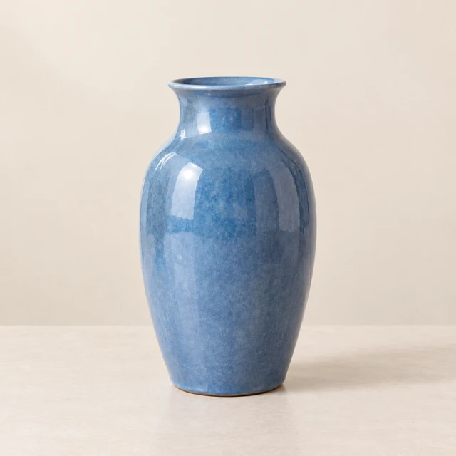 Matte blue ceramic vase on a clean neutral studio surface with a pale warm wall.