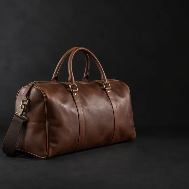 Leather duffel side-lit on a dark backdrop with open space.