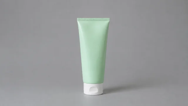 Mint cleanser tube standing on a quiet gray backdrop.