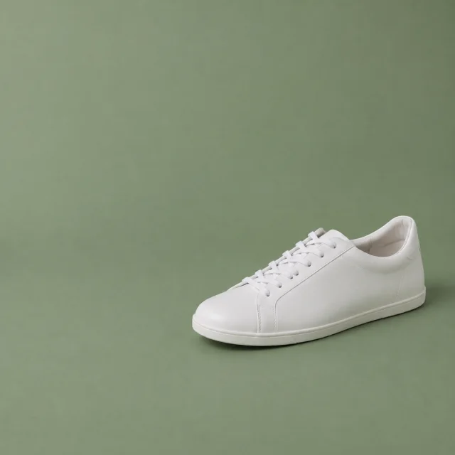 Plain white low shoe on a muted green background, with empty space beside it.