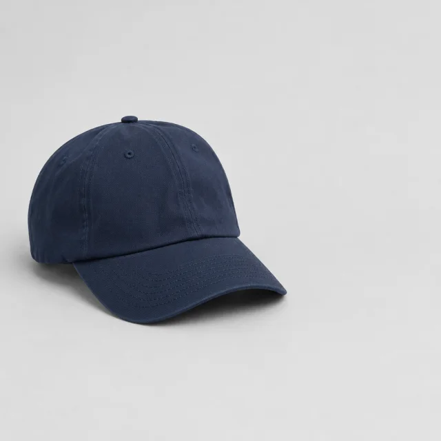 Plain navy baseball cap on a light gray background, with empty space beside it.