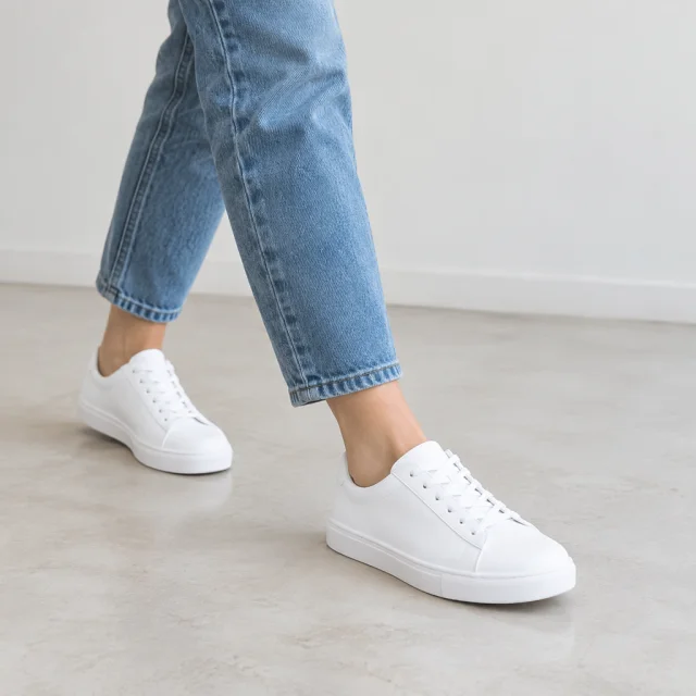 Plain white low shoes on a person's feet mid-step, with open floor around them.