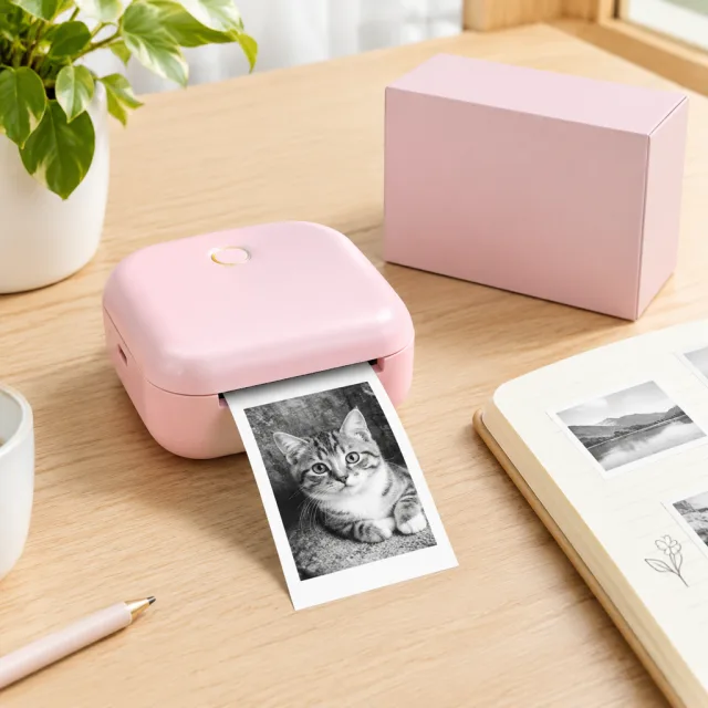 A creator prints photo stickers from a pink mini printer at her desk and peels the first print off the roll.