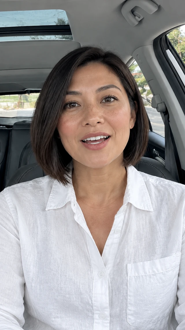 Adult Southeast Asian woman with short dark angled bob in a car setting, speaking to camera seated in the driver seat with hands resting low, speaking to camera.