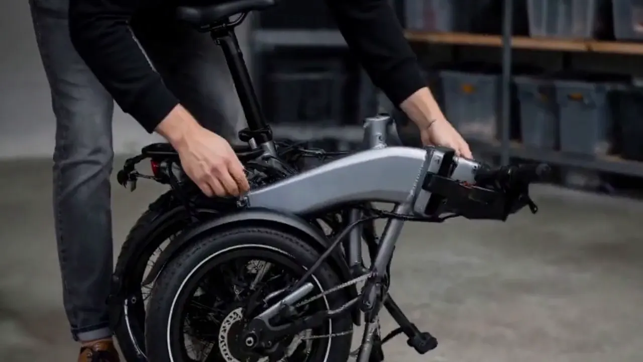 Hands unfold a black folding electric bicycle and inspect its hinge.
