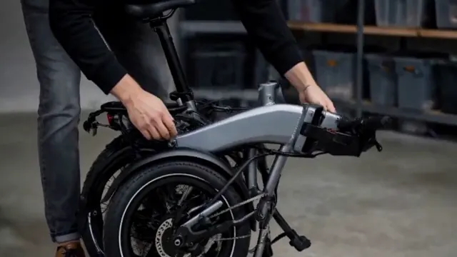 Hands unfold a black folding electric bicycle and inspect its hinge.