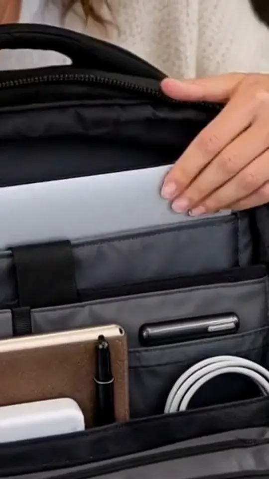 Hands open a black commuter backpack in a cafe, show its compartments, and put it on.
