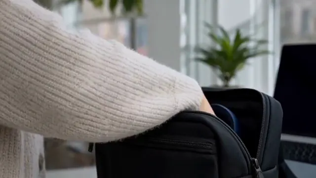 Hands inspect dark blue headphones and place them into a commuter bag.