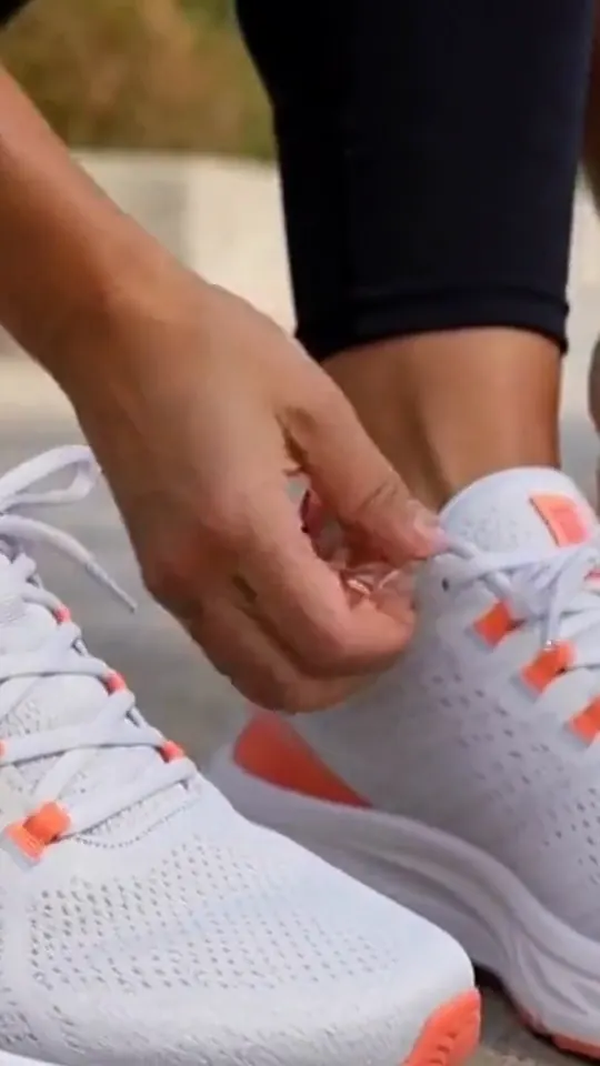 Hands tie white running shoes before feet run and show the soles.