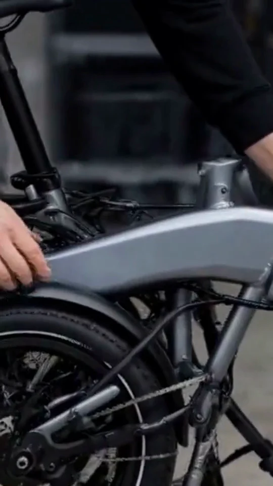 Hand checks the hinge on a gray folding electric bicycle.