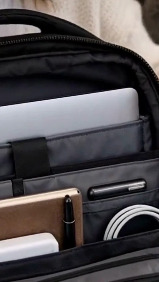 A person arranges a tablet and accessories in a black commuter bag.