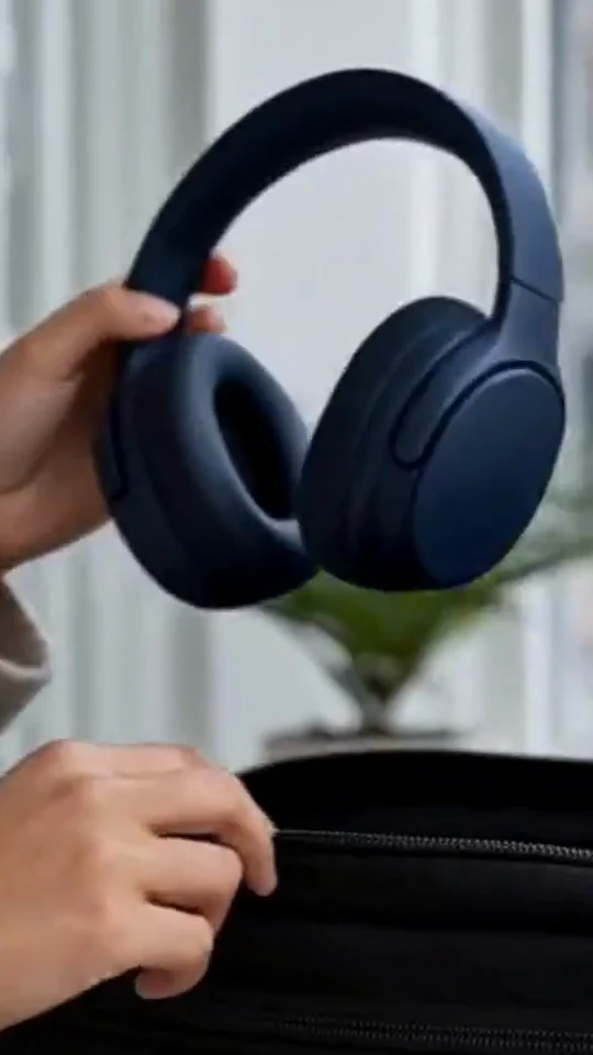 A hand holds dark blue over-ear headphones above an open black bag.
