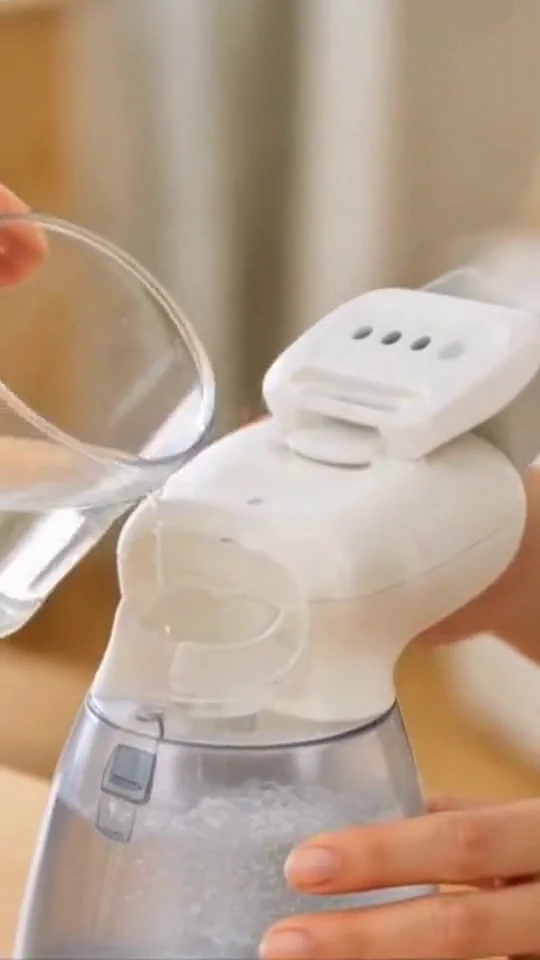 A hand fills a white garment steamer before use.