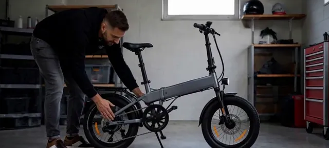 Person crouching to unfold a gray folding electric bike in a garage