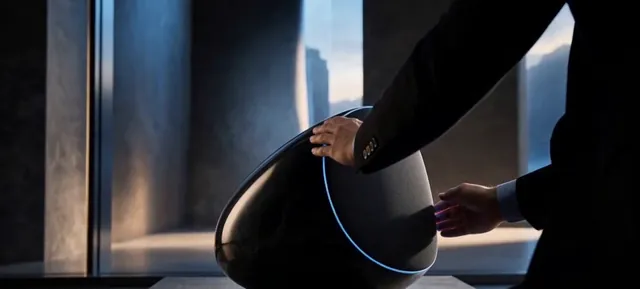 Person adjusting a black speaker with a blue light ring beside a large window