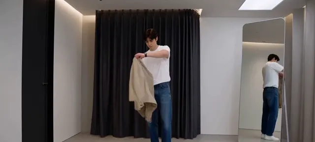 Person holding a beige overshirt in a fitting room with a mirror