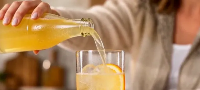 Golden sparkling drink poured from a glass bottle into a glass with ice and an orange slice