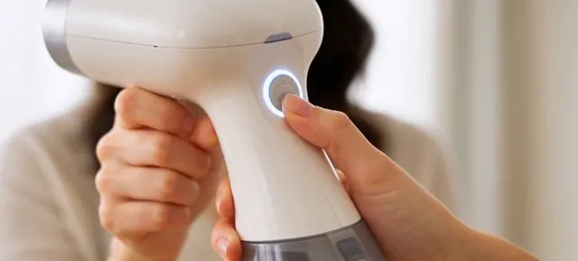 Close view of a handheld garment steamer and its glowing button