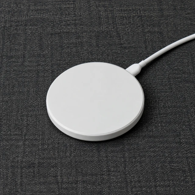 Simple round wireless charging pad on dark fabric with its cable visible, no phone.