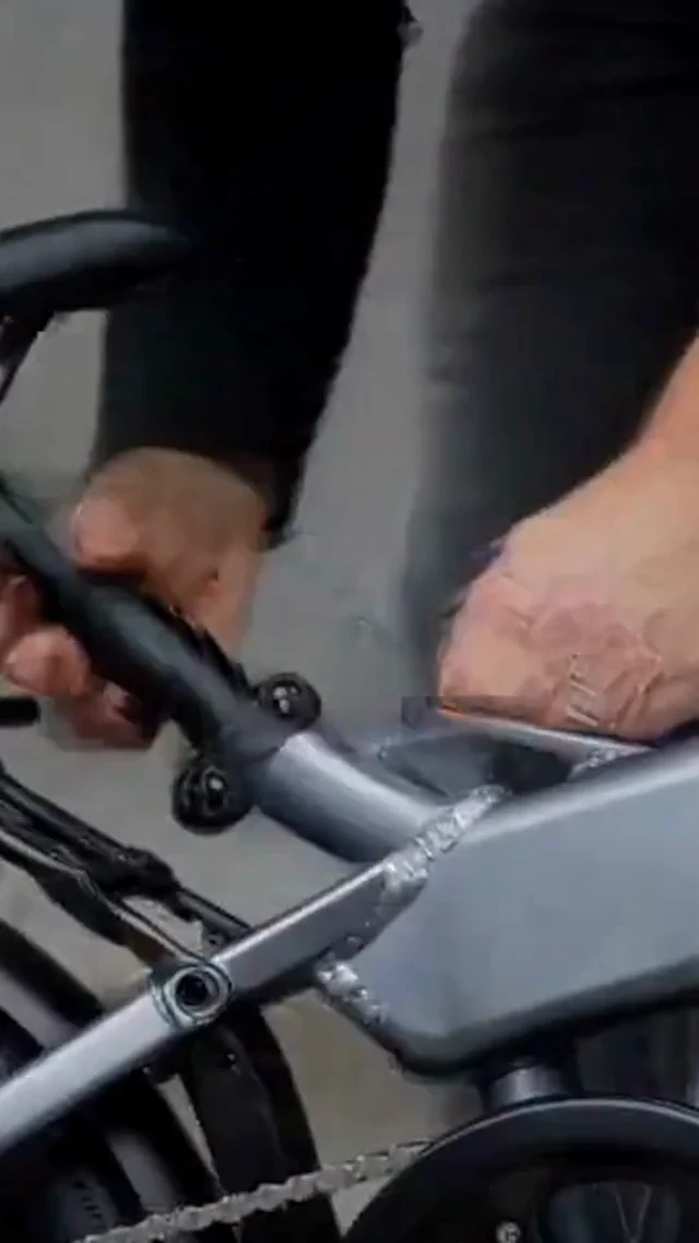 Hands inspect the hinge of a black folding bicycle in a vertical sale video frame.