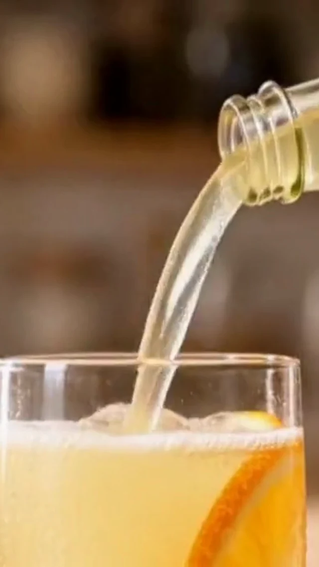 Citrus drink pours from a clear bottle into a glass in a vertical video frame.