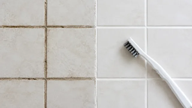 Bathroom tile grout with one half grimy and the other clean, a small grout brush resting on it.