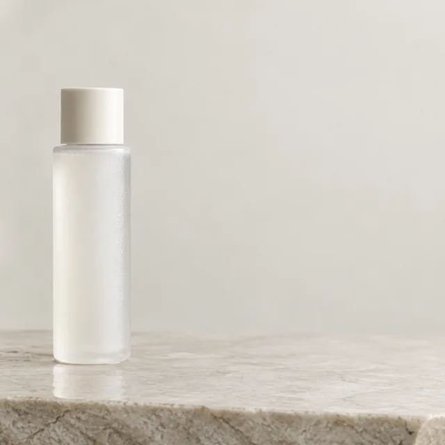 Skincare bottle on wet stone with open space beside it.