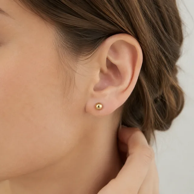 Close view of small gold stud earrings worn on the ear.