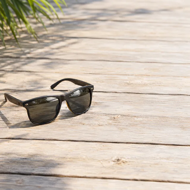 Sunglasses on a sun-bleached wooden deck with open space on the right.