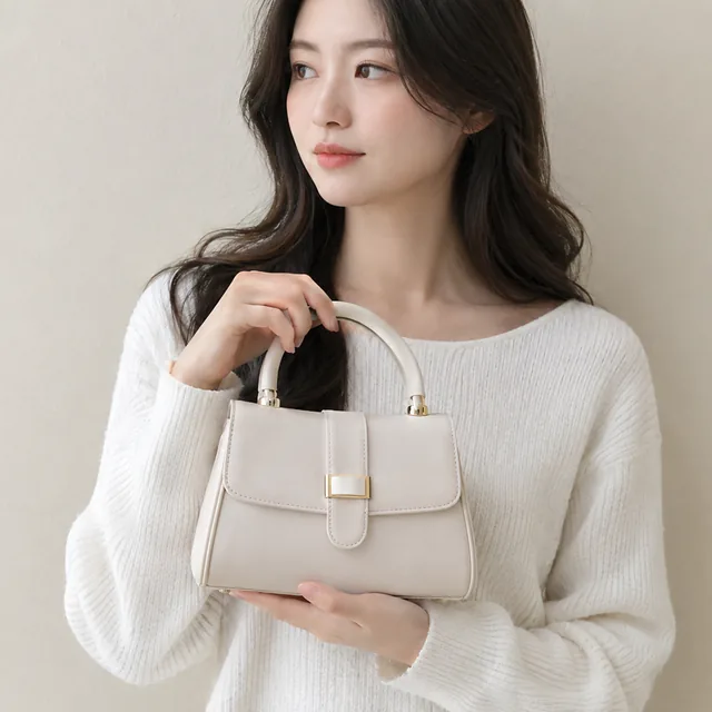 Person holding a small handbag at chest height against a plain wall.