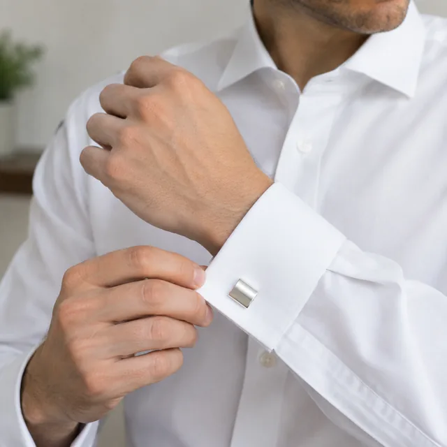 Silver cufflinks worn with a white shirt cuff, framed around the accessory.