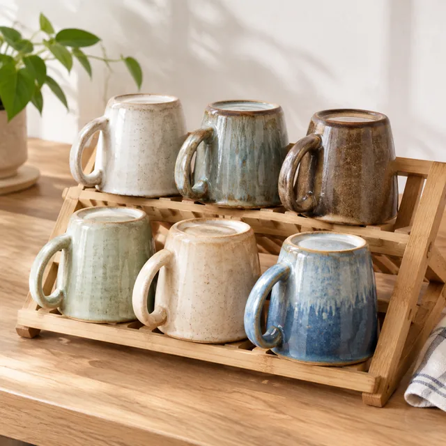 Handmade mugs lined up on a drying rack.