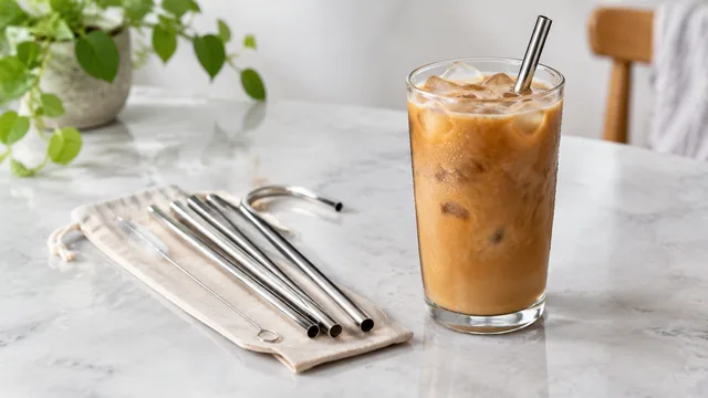 Reusable steel straw set beside an iced drink.