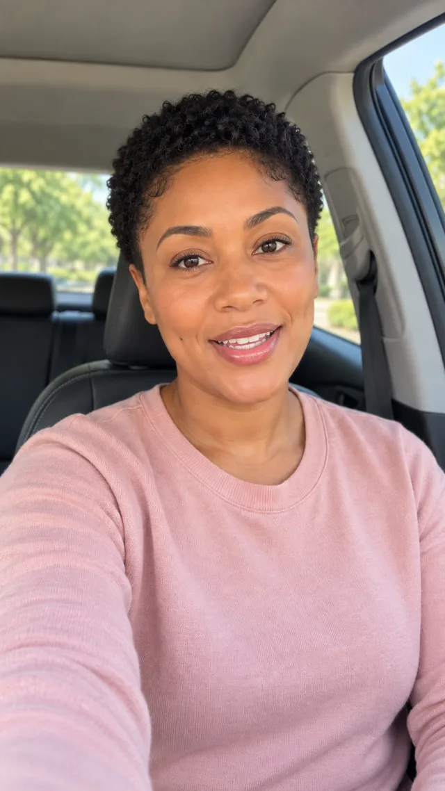 an adult Black woman with a tight short natural haircut in a car speaks to camera with empty hands.