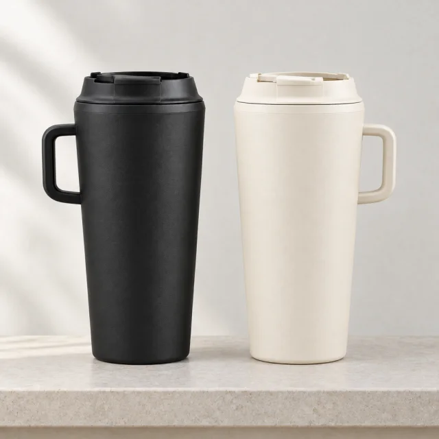The same matte black and warm cream insulated tumblers on a light stone shelf.