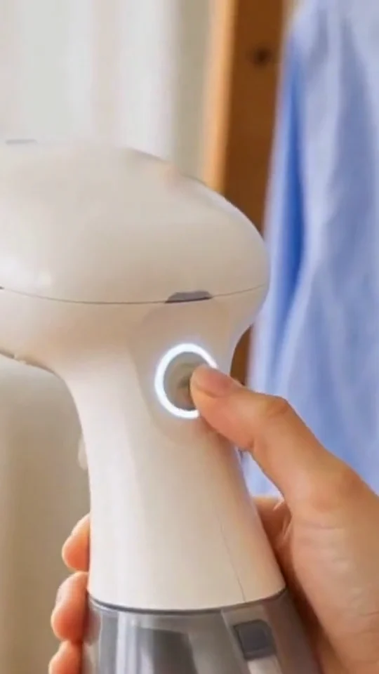 Hand switching on a white handheld garment steamer, its power button lit.