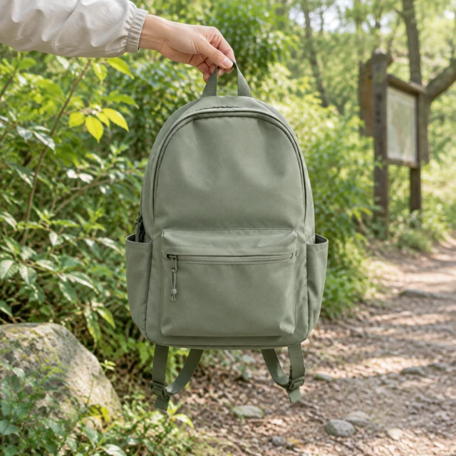 Small daypack lifted by its top handle near a trailhead.