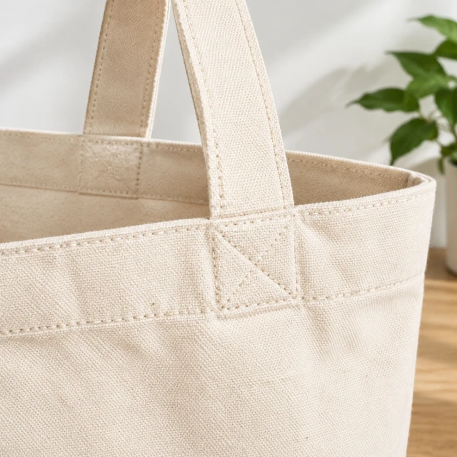 Close view of a plain canvas tote bag weave and stitched handle in natural light.