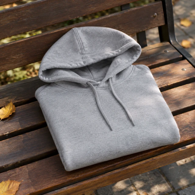 Plain gray cotton hoodie folded neatly on a park bench in soft daylight.