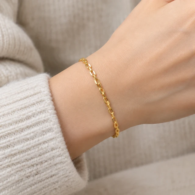 Plain gold bracelet on an adult wrist beside a neutral knit sleeve, close view.