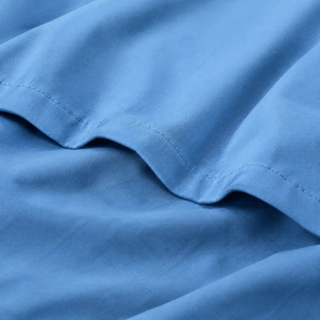 Close view of blue cotton fabric with visible plain stitching and soft folds.