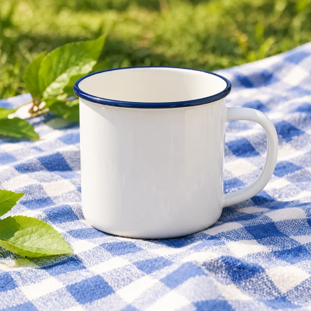 Plain enamel camping mug on a summer picnic blanket with a few leaves in the background.