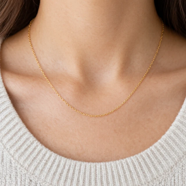 Fine gold chain necklace resting naturally against a neutral knit neckline, close product detail.