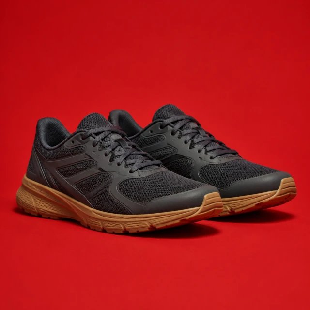 Dark mesh running shoes on a vivid red studio backdrop with clear open space.