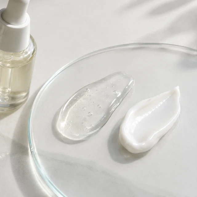 Clear serum and white cream swatches on glass beside a plain dropper bottle.