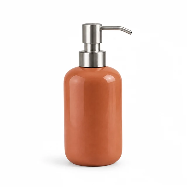 Unbranded ceramic soap dispenser in warm terracotta glaze with a brushed metal pump on white.