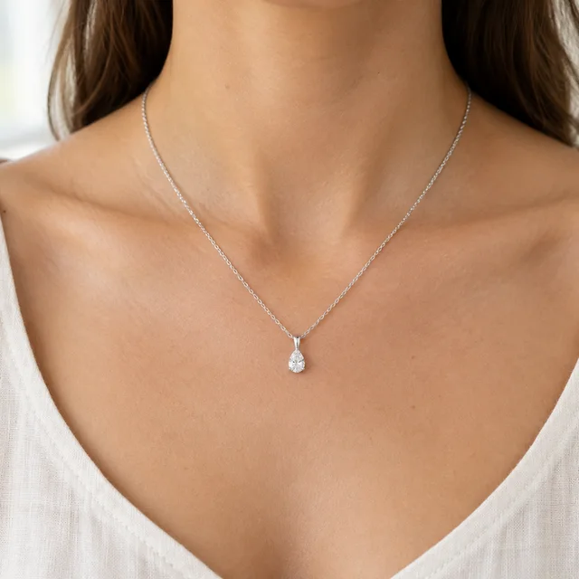 Silver teardrop pendant worn at the collarbone above an ivory linen neckline.