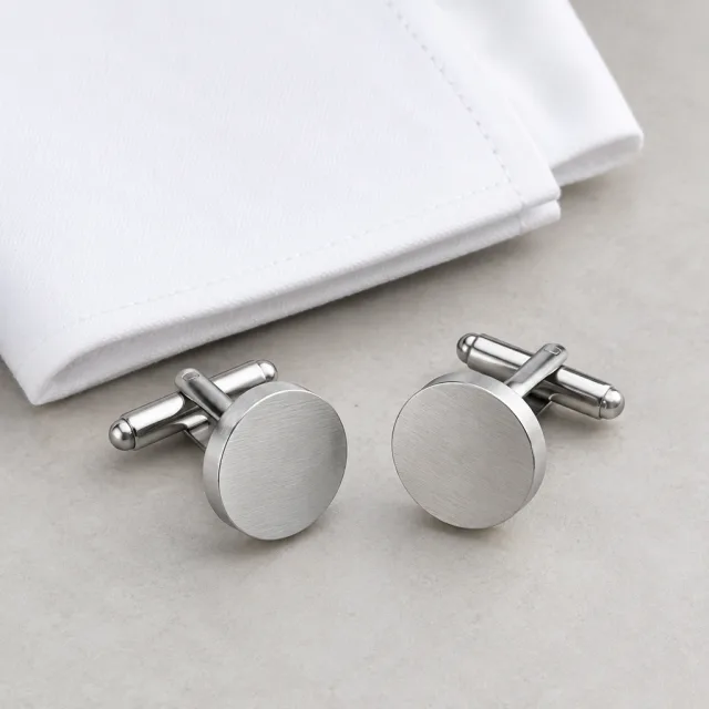 Pair of brushed-silver cufflinks beside a white shirt cuff.