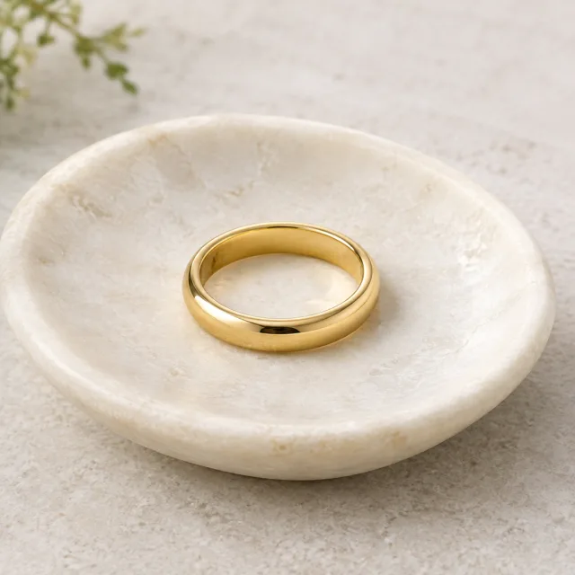 Plain polished gold band on an ivory stone dish.